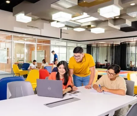 Grupo de estudiantes trabaja en equipo en un aula moderna y colorida, con computadoras portátiles.